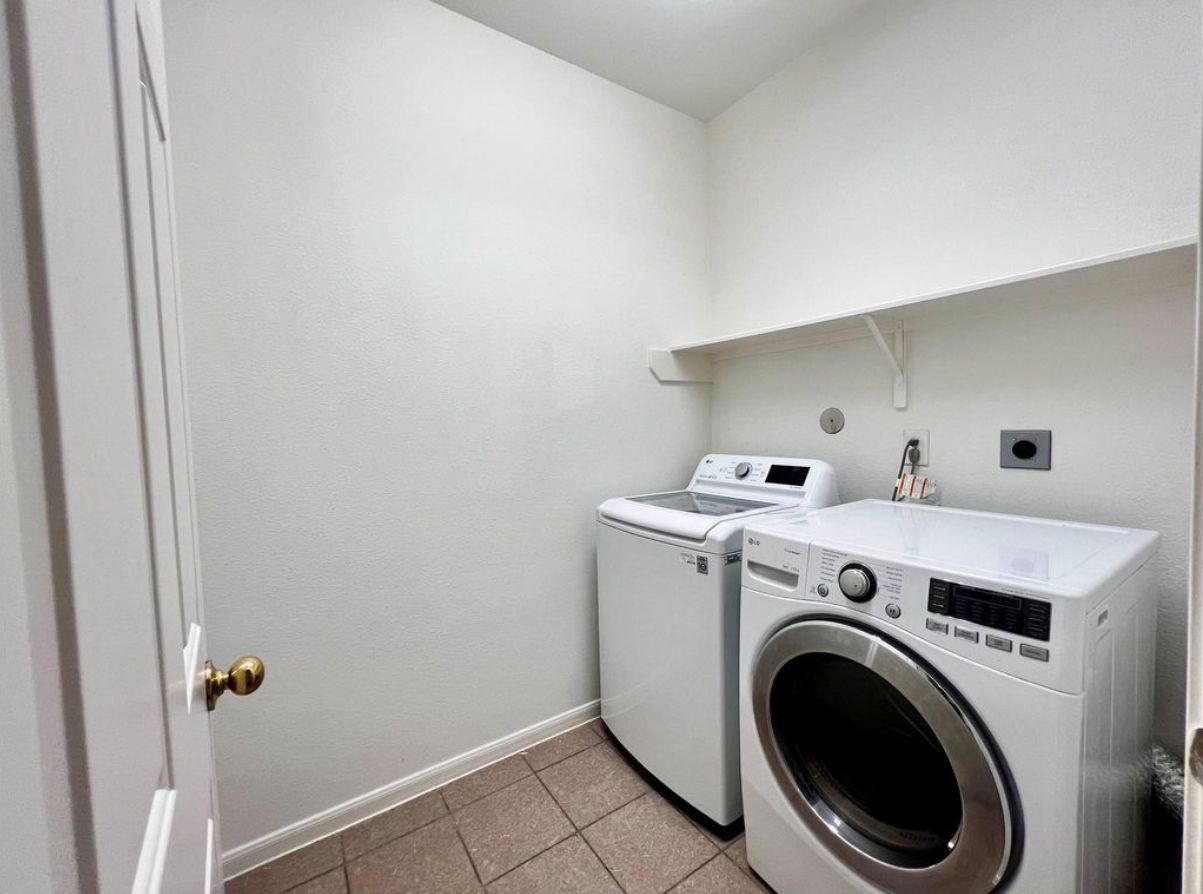 A laundry room with two washing machines and a dryer, a door, and a white wall.