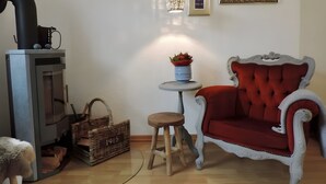 Et værelse med en pejs, en rød polstret stol, et lille bord med en plante og et billede i ramme på væggen.