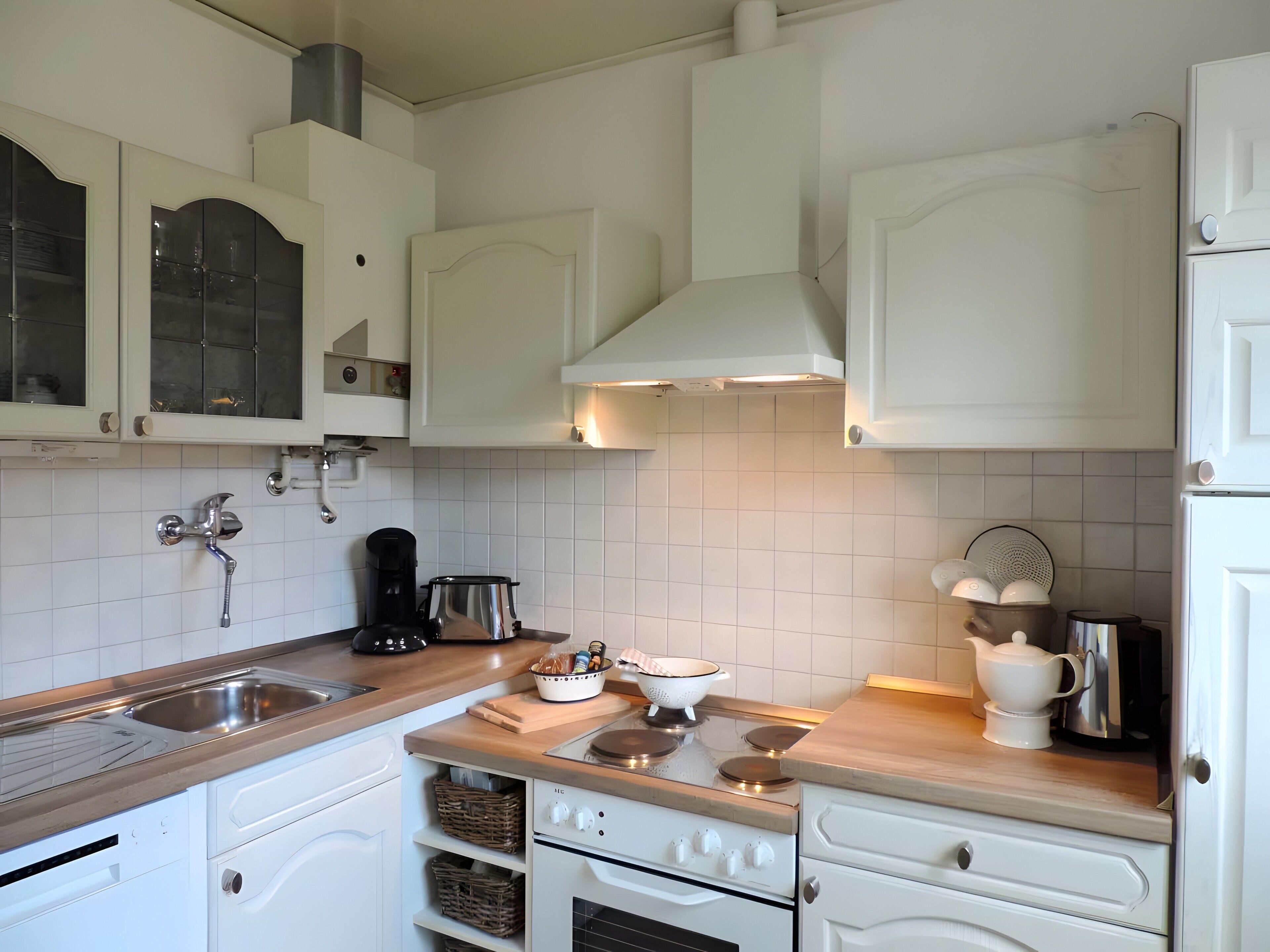 Een moderne keuken met witte kasten, een roestvrijstalen spoelbak, een koffiezetapparaat en een fornuis.