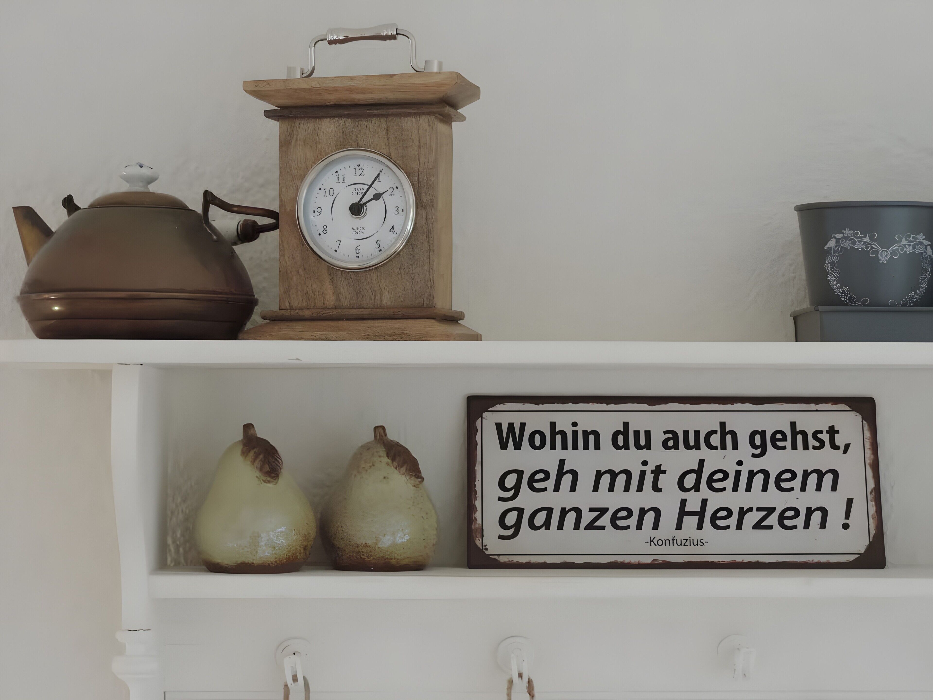 A shelf with a wooden clock, a teapot, two ceramic pears, and a sign with a quote.