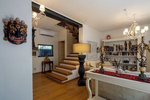 Eine Treppe führt zu einer zweiten Etage, eine Kristallleuchter, ein Bücherregal mit diversen Gegenständen und eine dekorative Maske an der Wand.
