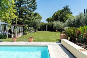 Ein Garten mit Schwimmbad, überdachter Terrasse und Schaukeln.