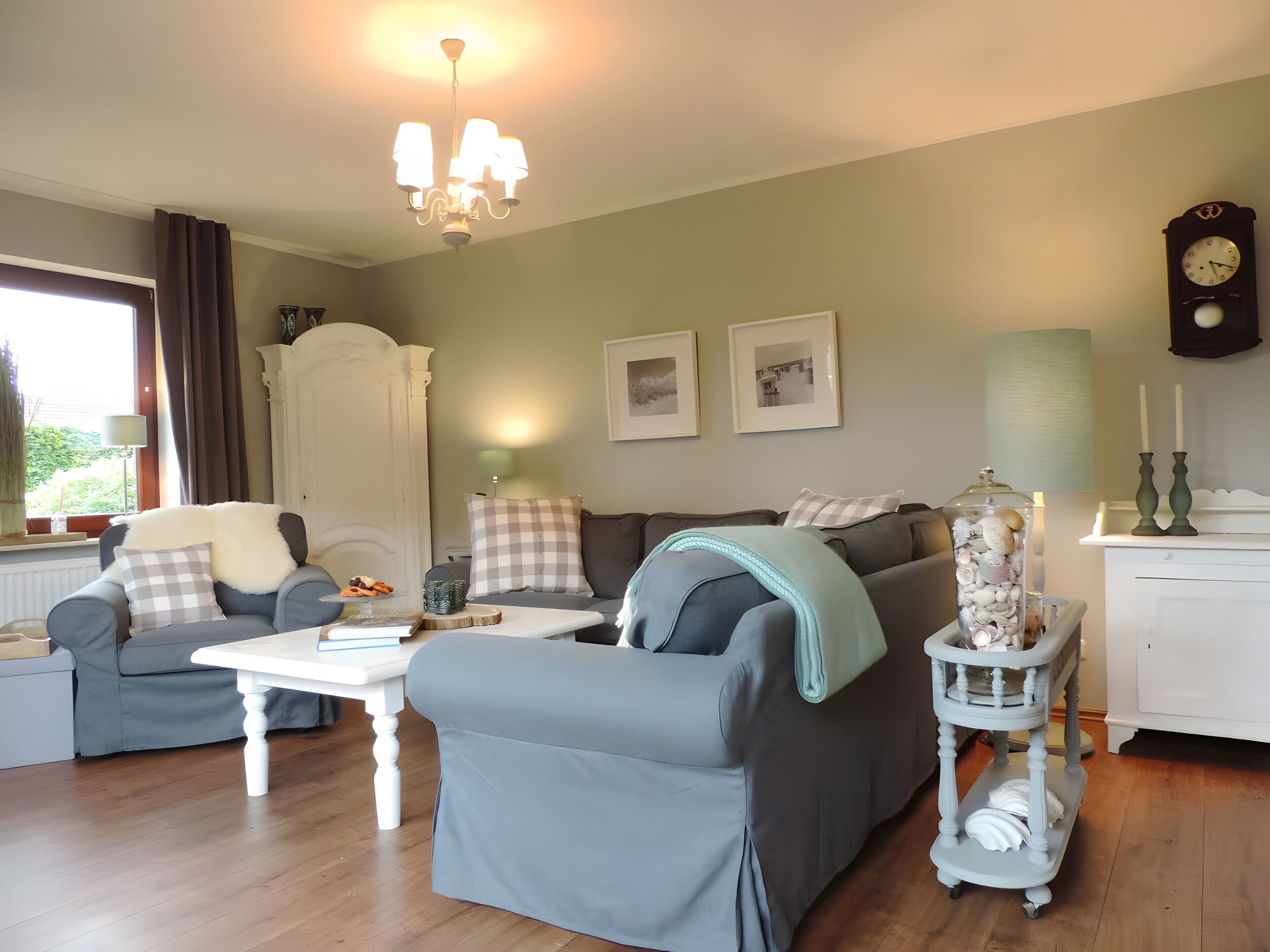 A living room with a chandelier, a sofa set, a coffee table, a side table with a lamp, and a clock on the wall.