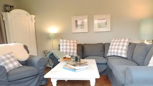 Un soggiorno con un divano grigio, un tavolino da caffè bianco con libri e un oggetto decorativo, e due quadri appesi al muro.