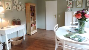 Zona pranzo con tavolo bianco, sedie, un lampadario, una libreria e una porta.