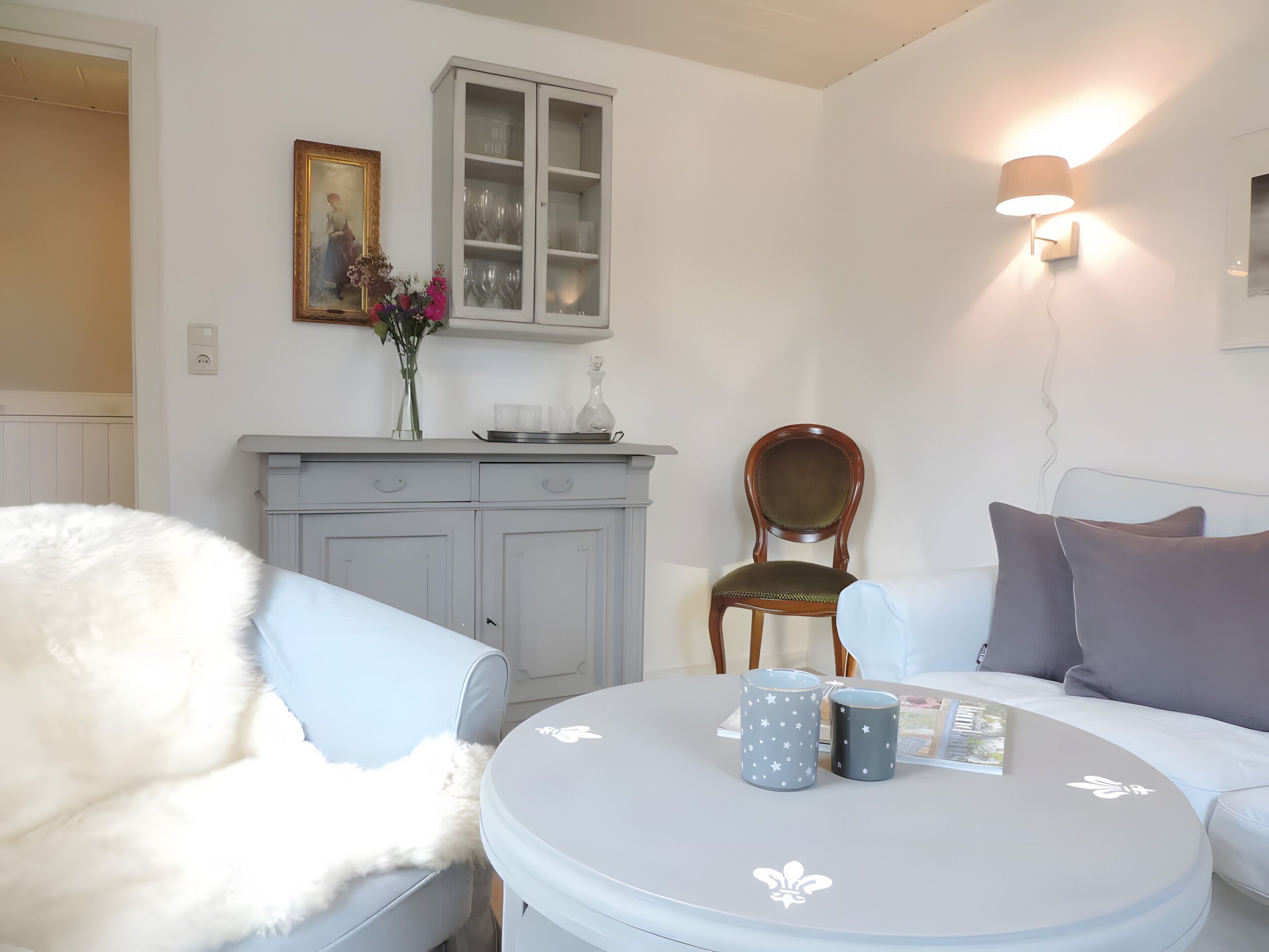 Una habitación con una mesa redonda, dos sillas, un armario, una lámpara de pared y un cuadro enmarcado.