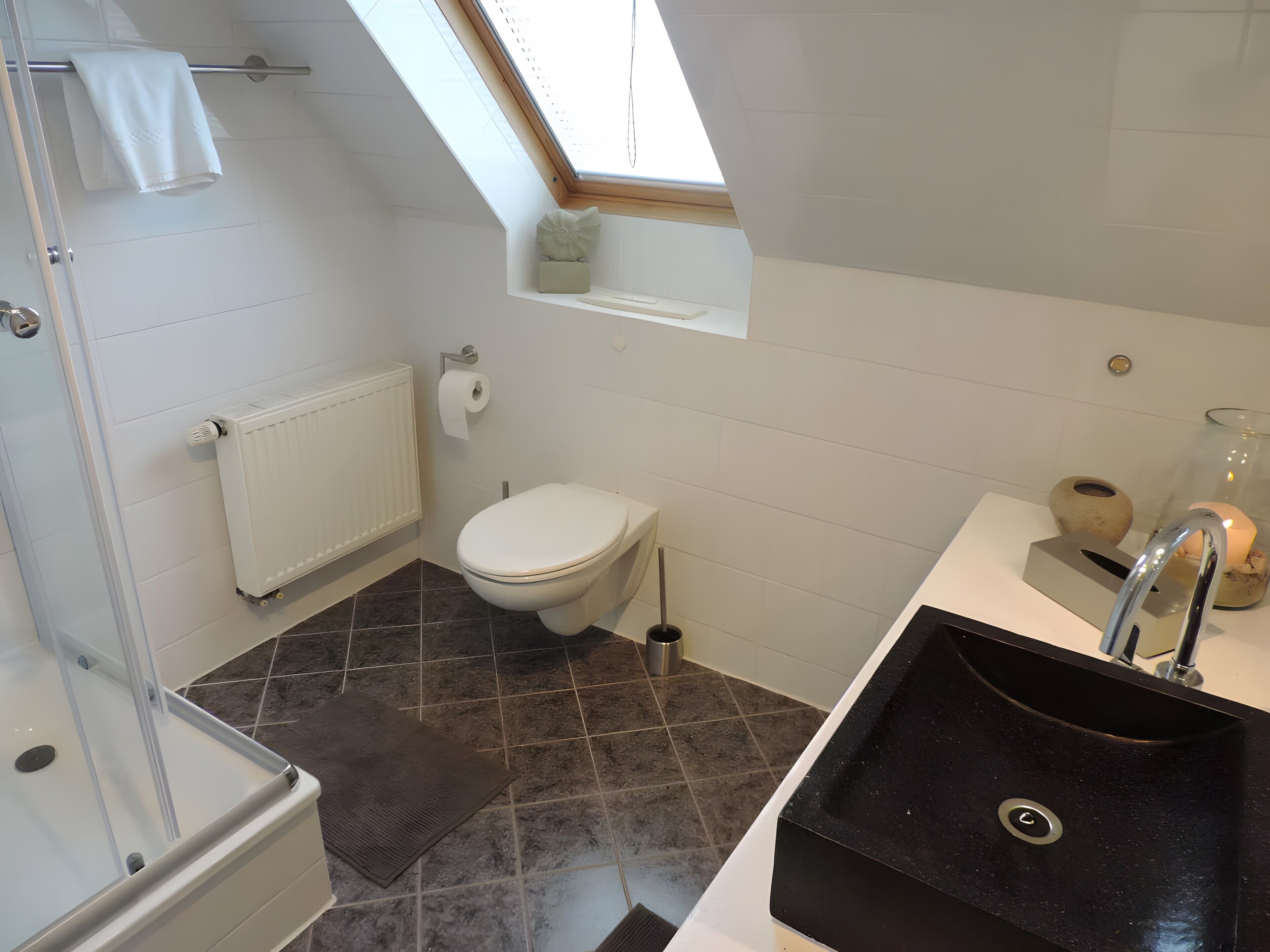 Ein modernes Badezimmer mit Oberlicht, Toilette, Waschbecken und Duschbereich.