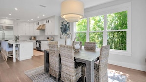 A modern kitchen with white cabinets, a central island, and a dining area with wicker chairs. - Captain's Quarters Longboat Key (Longboat Key)