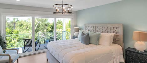 Een slaapkamer met een groot bed, een nachtkastje, een stoel en een balkon met uitzicht op groen.