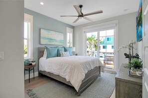 Ein Schlafzimmer mit Bett, Deckenventilator, einem Gemälde und Blick ins Freie.