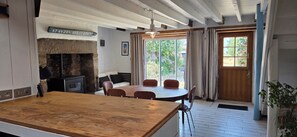 Una cocina con chimenea de piedra, una mesa de comedor con sillas, una encimera de madera y vistas a través de una ventana con cortinas.