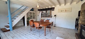 A dining area with a wooden table and chairs, a staircase, a kitchen area, and a stone wall.