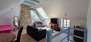 Una sala de estar con pared de piedra, un sofá, un televisor sobre un mueble de madera y una escalera con barandillas azules.