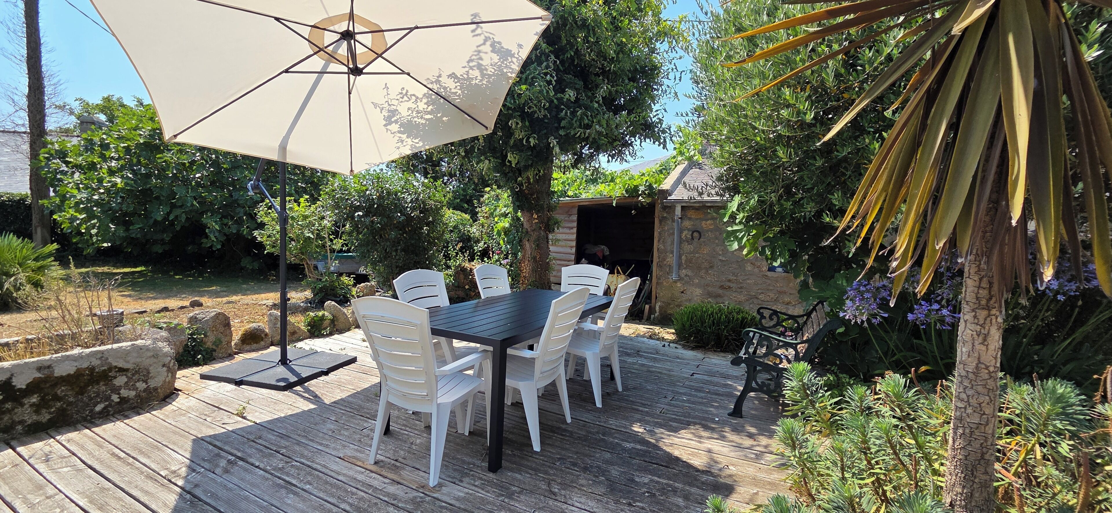 Una terraza de madera con una mesa, sillas y una sombrilla, con una estructura de piedra al fondo.