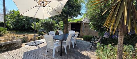 Una terraza de madera con una mesa, sillas y una sombrilla, con una estructura de piedra al fondo.