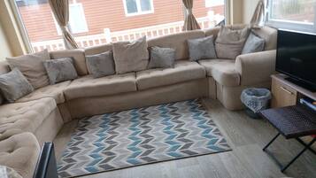 Una sala de estar con un sofá modular, un televisor de pantalla plana y una alfombra estampada.