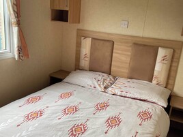 Una cama individual con cabecera de madera, una mesita de noche y una pequeña estantería sobre la cama.