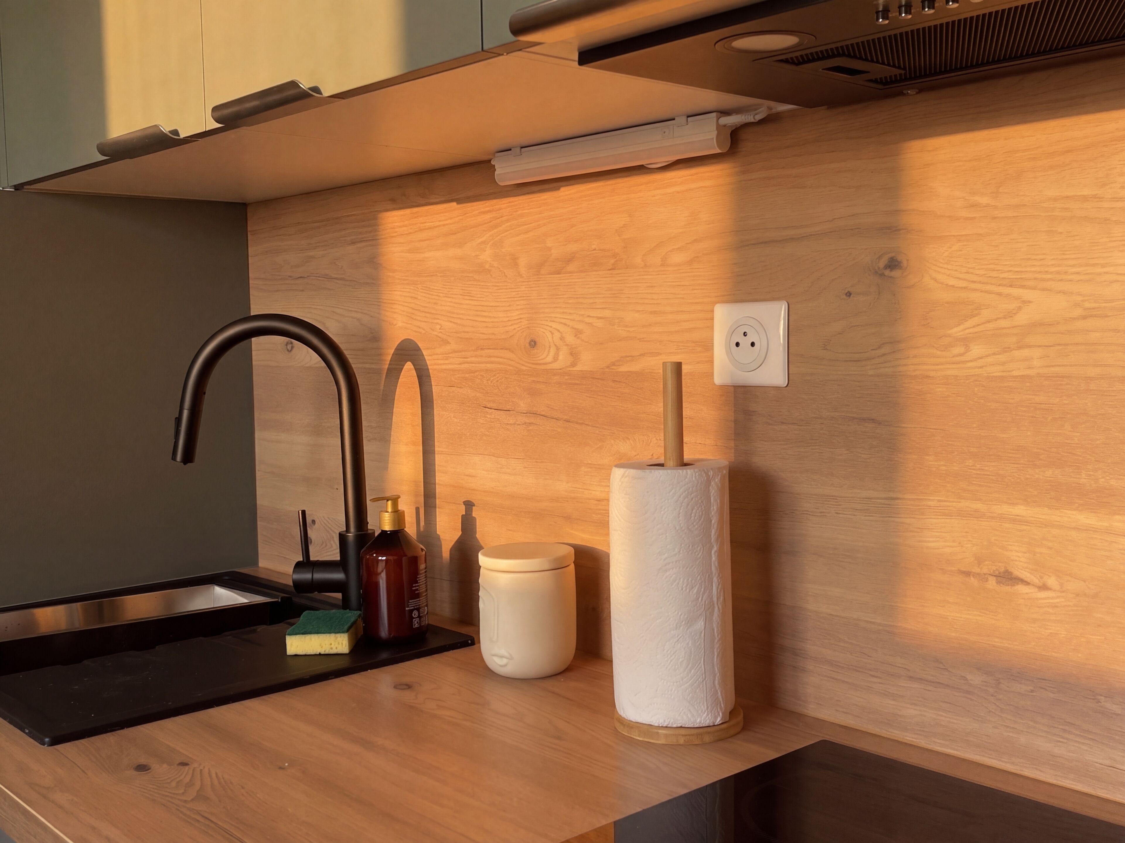 Uma cozinha moderna com pia preta, torneira, porta-papel toalha e bancada de madeira.