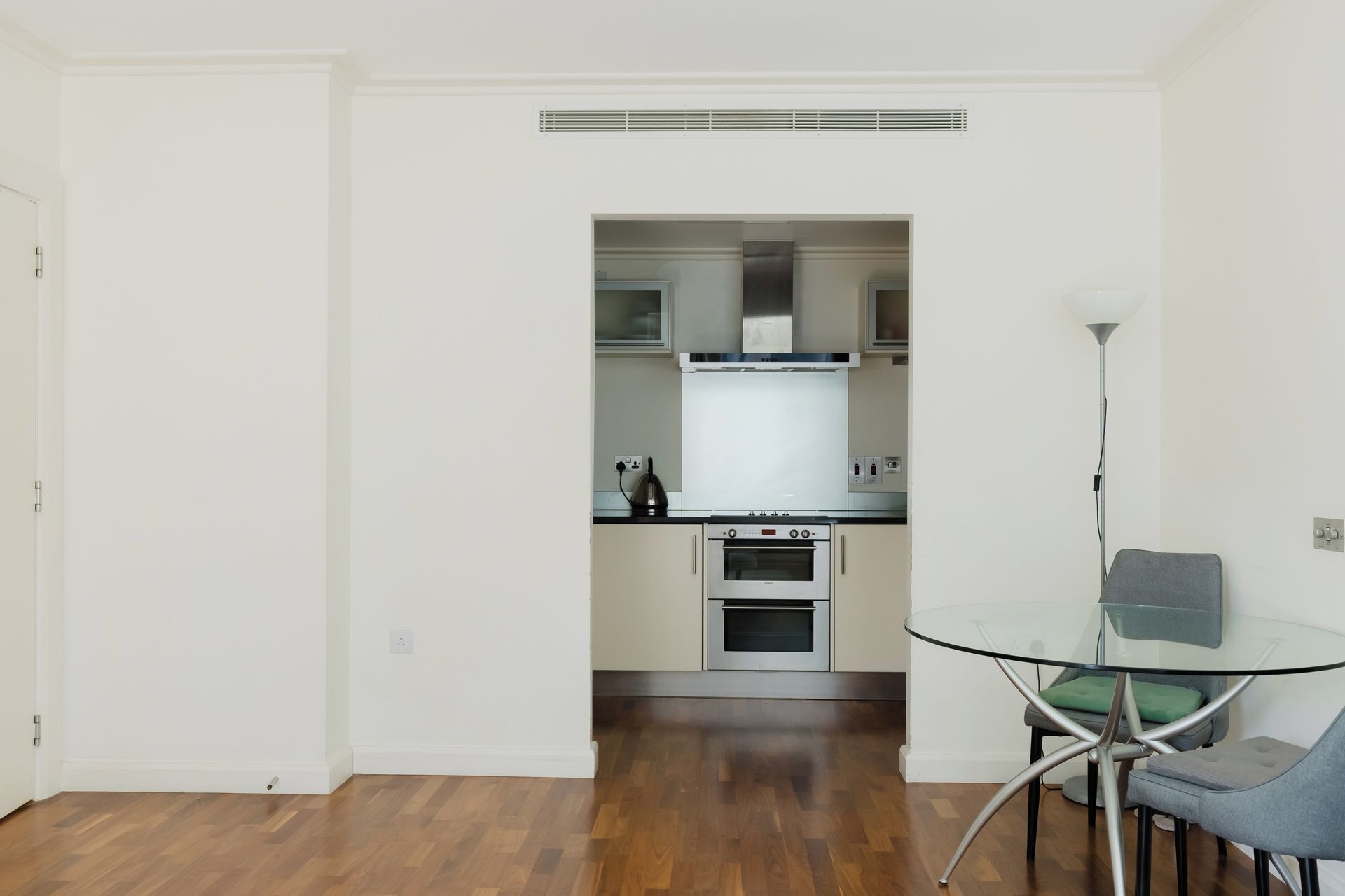 A modern kitchen with a built-in oven and a dining area with a glass table and chairs.
