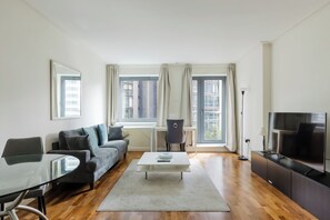 A modern living room with a sofa, coffee table, TV, and a dining area with a glass table. - Sleek 1BDR City Stay In Canary Wharf (Greater London)