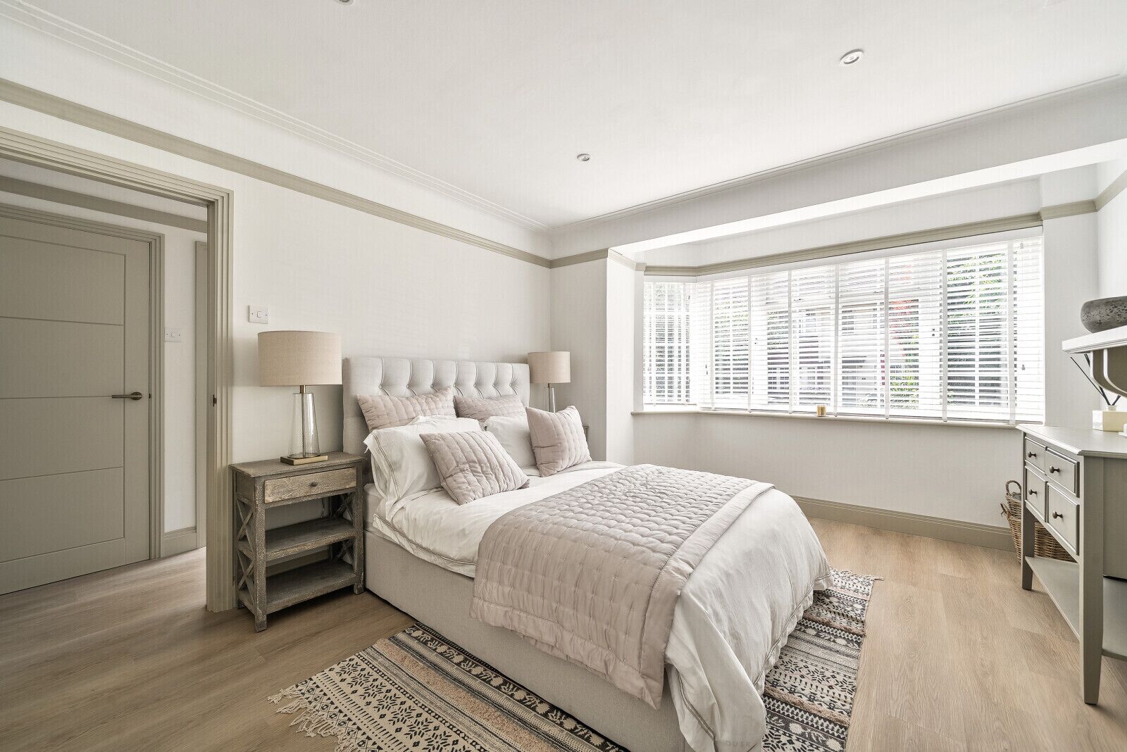 Une chambre à coucher avec un lit, des tables de chevet, une fenêtre avec des stores et une porte.