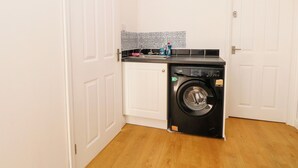 Ein kleiner Waschraum mit einer Waschmaschine mit Frontlader, einem Waschbecken und einer gefliesten Spritzschutzwand.