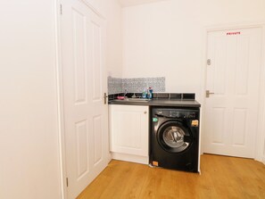 A compact laundry room with a front-loading washing machine, a sink, and a tiled backsplash. - 33 North Denes (Great Yarmouth)