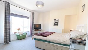 Ein Schlafzimmer mit einem Bett, einem Fernseher, einem Heizkörper und einem Fenster mit Vorhängen.