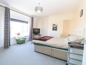 A bedroom with a bed, a television, a radiator, and a window with curtains. - 33 North Denes (Great Yarmouth)