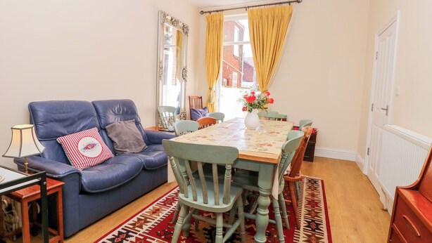 Ein Wohnzimmer mit einem blauen Sofa, einem Esstisch und einem gemusterten Teppich.