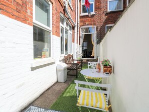 Ein kleiner Patio-Bereich mit einer weißen Bank, einem Tisch mit zwei Weingläsern und einer Weinflasche.