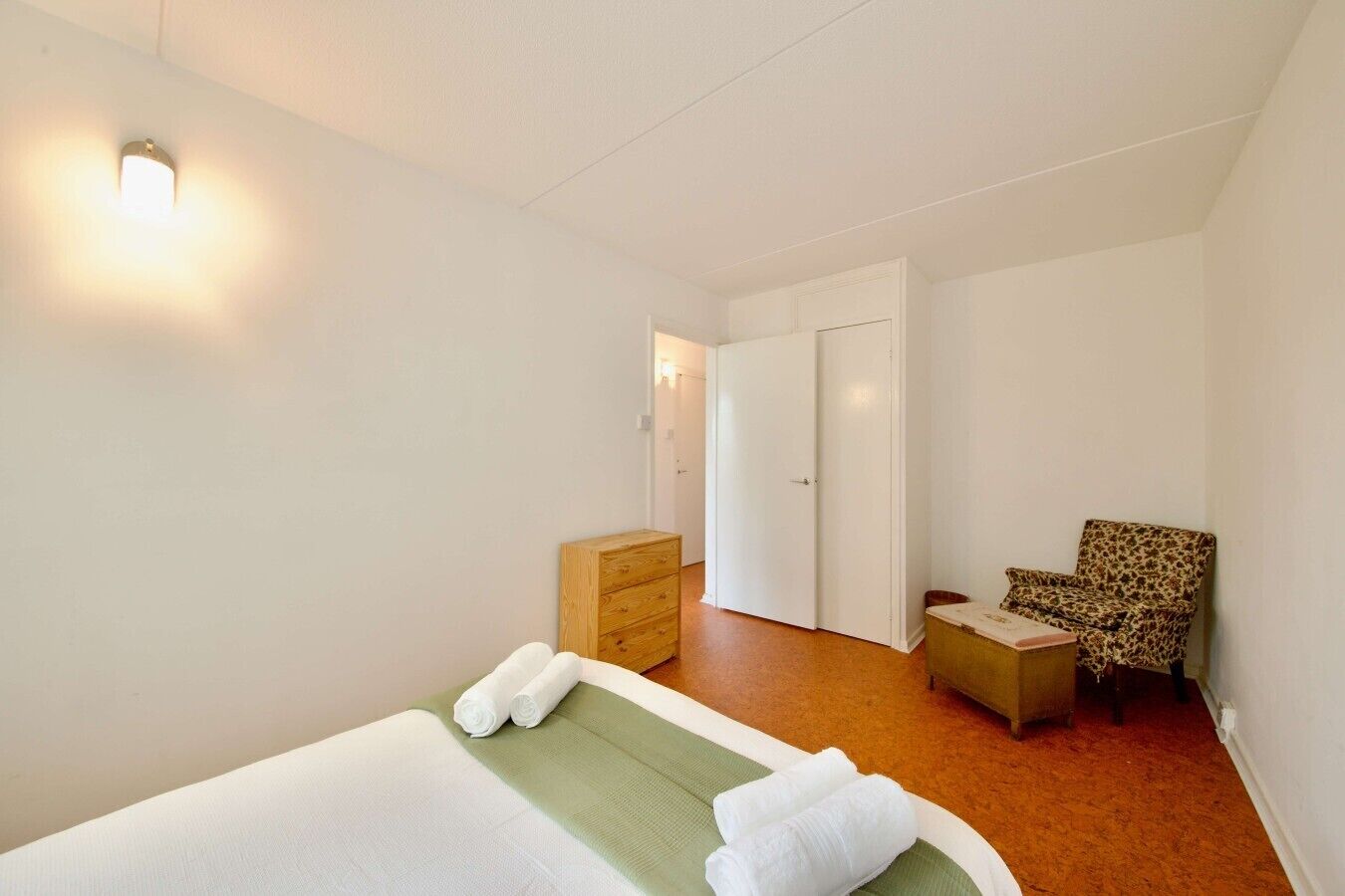 Ein Hotelzimmer mit einem Bett, einer grünen Matte, einer Holzkonstruktion, einem Sessel mit Leopardenmuster und einer weißen Tür.
