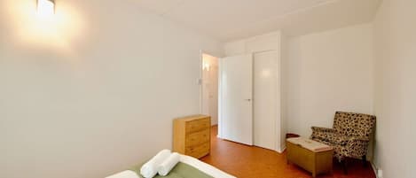 A hotel room with a bed, a green mat, a wooden chest, a leopard print chair, and a white door.