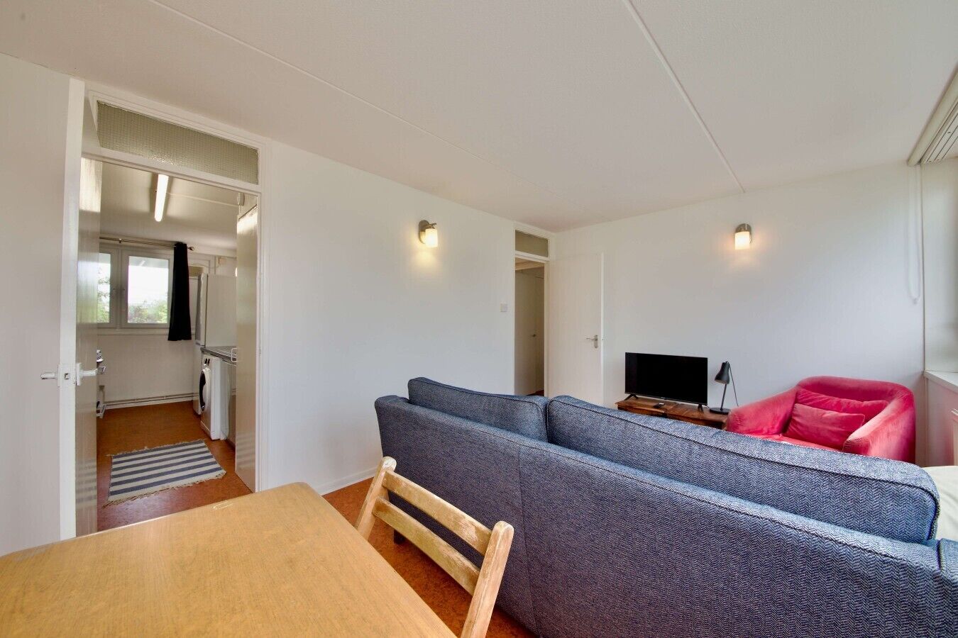 A compact living space with a sofa, a television, and a red chair. A wooden table is in the foreground.