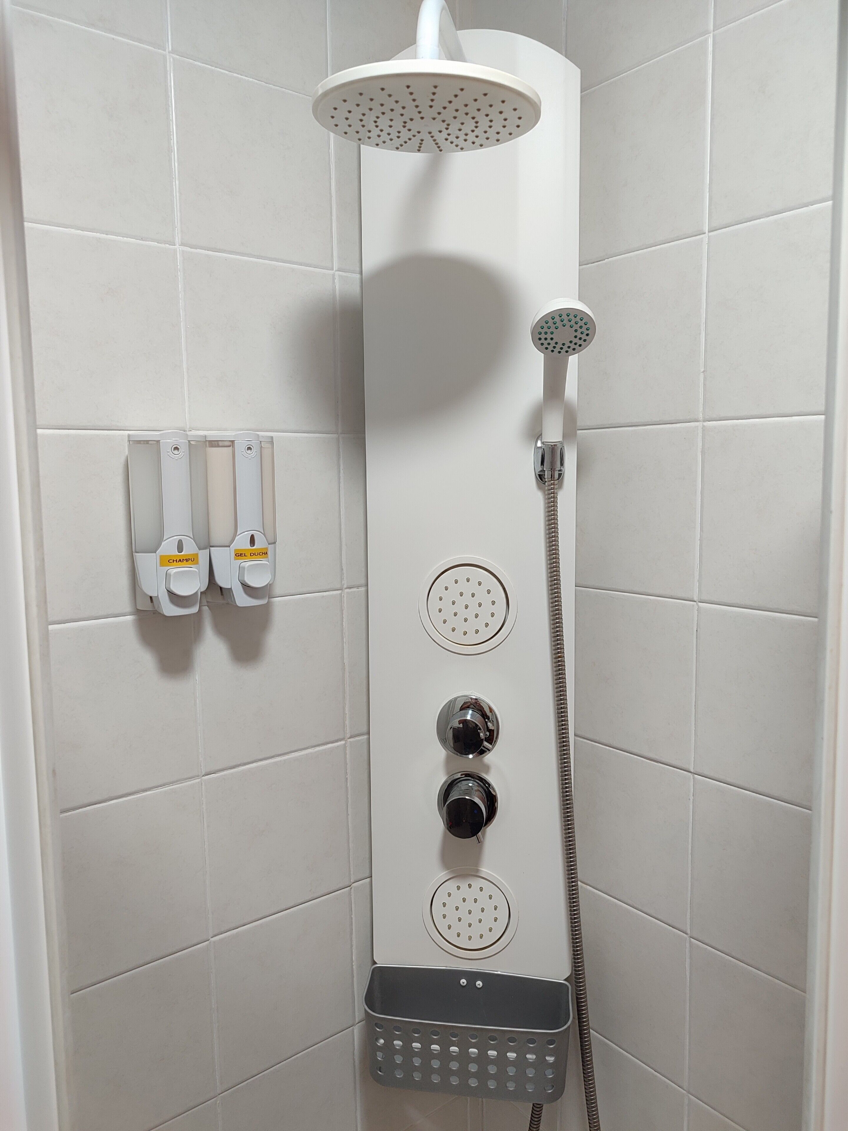 Een douche met een handdouche, een douchekop aan de muur en twee bedieningsknoppen.