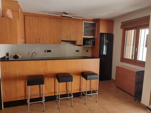A kitchen with wooden cabinets, a black refrigerator, a microwave, and three bar stools.