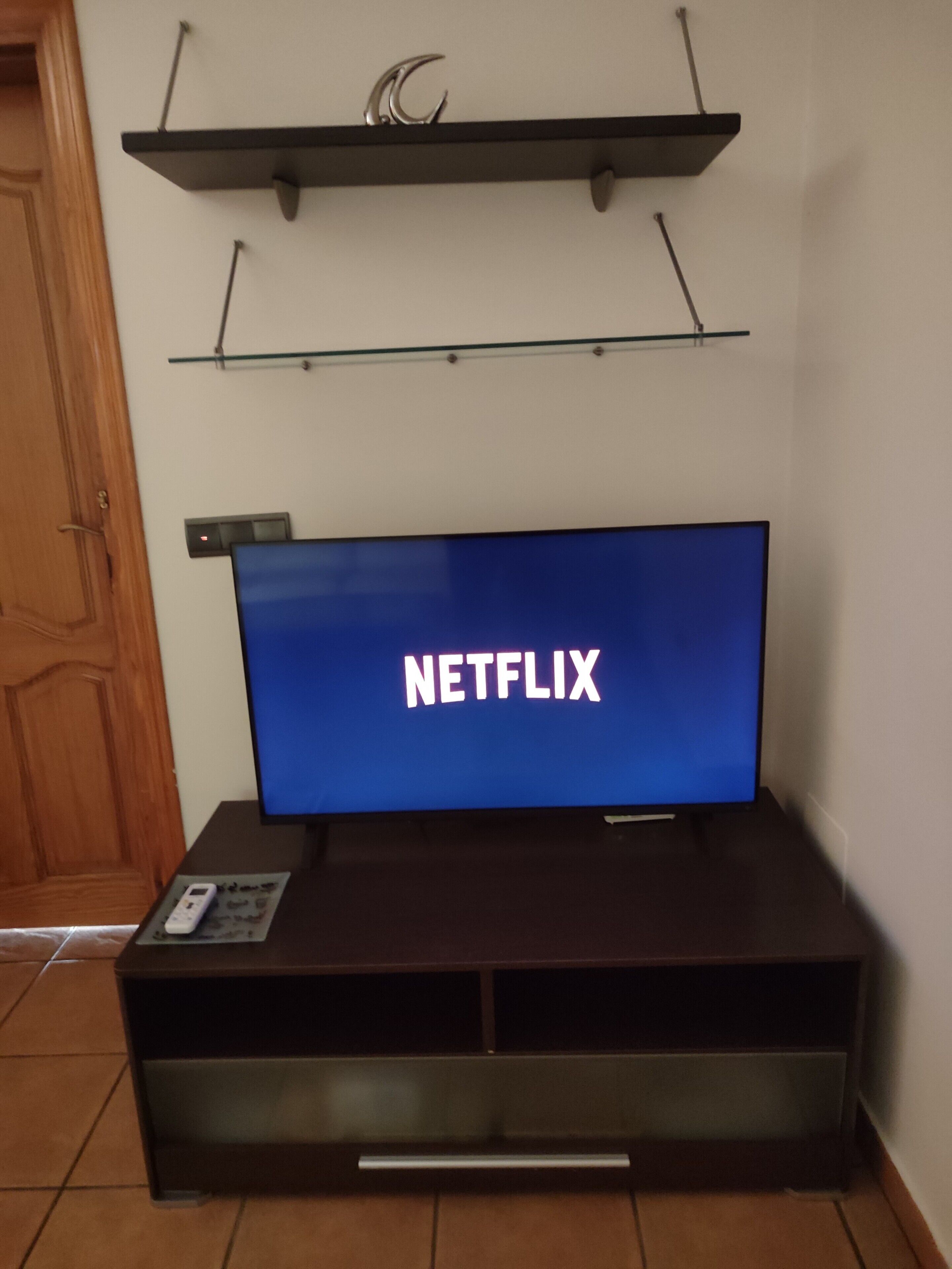 Een televisie met een Netflix logo op het scherm, bevestigd aan een muur boven een donker houten tv-meubel.
