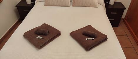 A neatly made bed with two towels and a bottle of lotion.