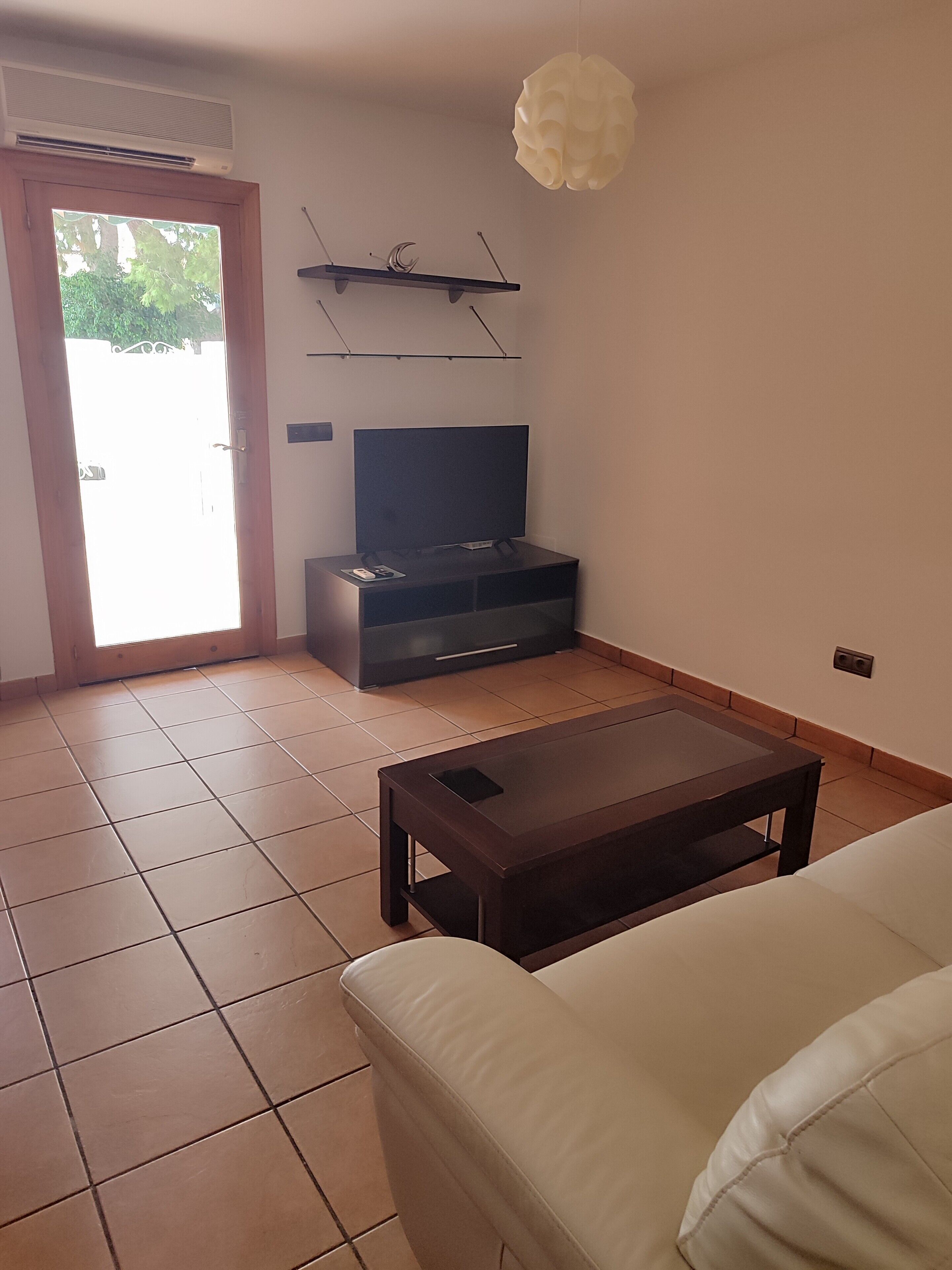 Een woonkamer met een bank, een salontafel, een televisie op een dressoir, een plafondventilator en een deur naar buiten.