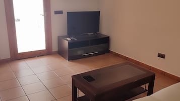 Een woonkamer met een bank, een salontafel, een televisie op een dressoir, een plafondventilator en een deur naar buiten.