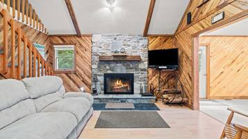 Un salon chaleureux avec une cheminée en pierre, un canapé, un téléviseur et des murs en bois.