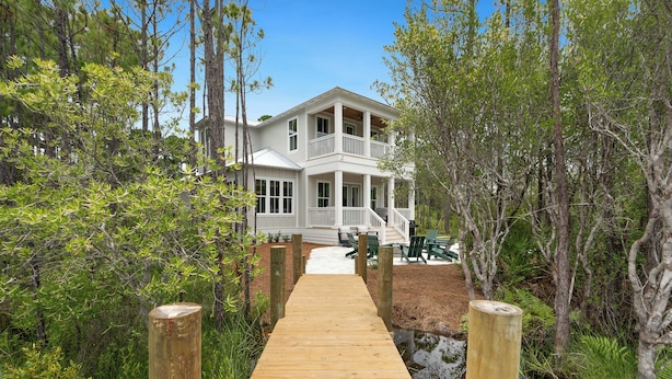 A two-story house with a porch, a wooden deck leading to it, and surrounding greenery. - NEW! 30A Home! Dock, Golf Cart, Putting Green, Community Pool & 4 Bikes (Santa Rosa Beach)