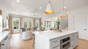 A spacious kitchen with a large island, a dining area with a sofa and chairs, and a staircase leading to an upper level. - NEW! 30A Home! Dock, Golf Cart, Putting Green, Community Pool & 4 Bikes (Santa Rosa Beach)