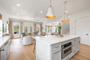 A spacious kitchen with a large island, a dining area with a sofa and chairs, and a staircase leading to an upper level. - NEW! 30A Home! Dock, Golf Cart, Putting Green, Community Pool & 4 Bikes (Santa Rosa Beach)