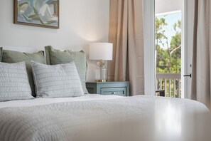 A neatly made bed with pillows, a bedside table with a lamp, and a view of greenery through a window. - NEW! 30A Home! Dock, Golf Cart, Putting Green, Community Pool & 4 Bikes (Santa Rosa Beach)