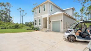 A two-story house with a garage, a covered driveway, and a golf cart parked in the driveway. - NEW! 30A Home! Dock, Golf Cart, Putting Green, Community Pool & 4 Bikes (Santa Rosa Beach)