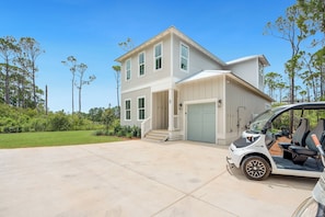 A two-story house with a garage, a covered driveway, and a golf cart parked in the driveway. - NEW! 30A Home! Dock, Golf Cart, Putting Green, Community Pool & 4 Bikes (Santa Rosa Beach)
