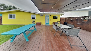 A covered patio with a wooden deck, a turquoise picnic table, and a dining table with chairs. - Al & Sherry's Oasis | Pet-Friendly Dream! (Rockport)