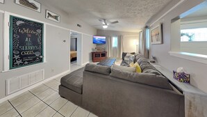 A living room with a large grey sectional sofa, a flat-screen TV mounted on the wall, and a ceiling fan. - Al & Sherry's Oasis | Pet-Friendly Dream! (Rockport)