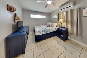 Quarto com cama, cômoda, escrivaninha, luminária e ar condicionado.